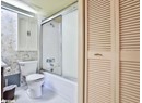 Bathroom featuring a closet, wallpapered walls, toilet, bath / shower combo with glass door, and tile patterned flooring