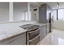 Kitchen featuring stainless steel appliances, gray cabinetry, ornate columns, and light stone counters