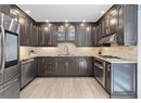 Kitchen with stainless steel appliances, a sink, under cabinet range hood, light stone countertops, and backsplash