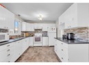 Kitchen featuring white appliances, under cabinet range hood, a sink, dark countertops, and backsplash