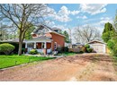 View of front of home with dirt driveway, brick siding, a porch, a garage, and a gate