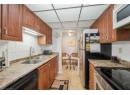 Kitchen featuring decorative backsplash, brown cabinets, white microwave, dishwasher, and light stone counters