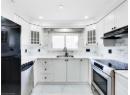 Kitchen featuring appliances with stainless steel finishes, glass insert cabinets, decorative backsplash, and light marble finish flooring