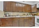 Kitchen featuring backsplash, white appliances, brown cabinetry, and light stone countertops