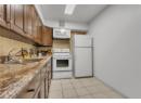 Kitchen with white appliances, decorative backsplash, light stone countertops, light tile patterned floors, and brown cabinets