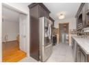 Kitchen with light stone counters, stainless steel appliances, dark brown cabinetry, light marble finish floors, and backsplash