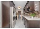 Kitchen with dark brown cabinets, stainless steel appliances, light marble finish flooring, light stone countertops, and backsplash